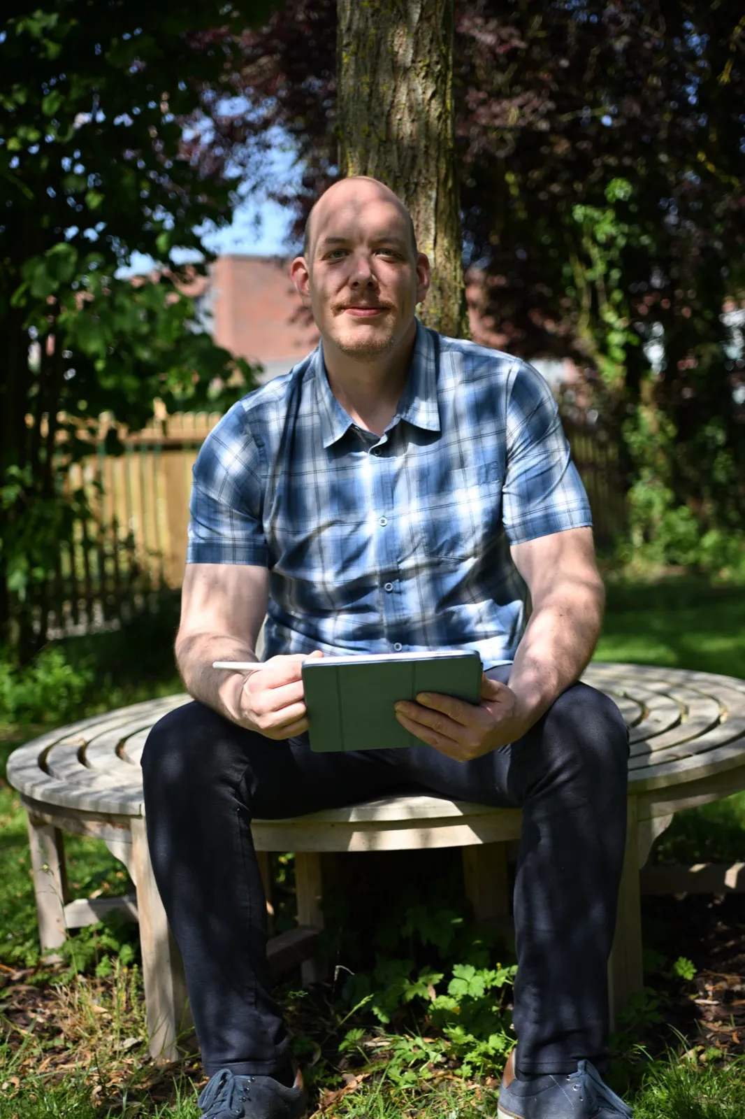 Dustin Dondrup sitzt mit Tablet auf einer Gartenbank