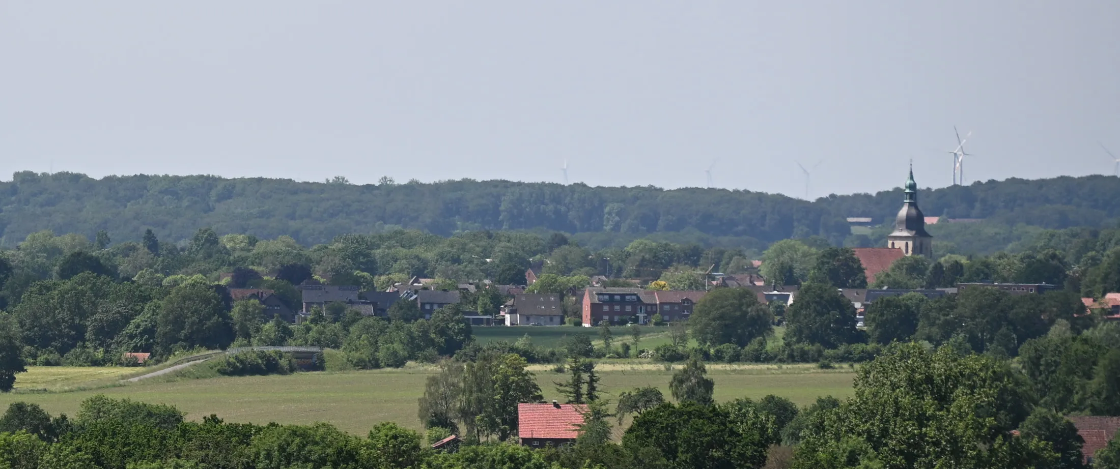 Blick über Felder auf Nottuln mit dem Turm der Pfarrkirche, dahinter Windräder