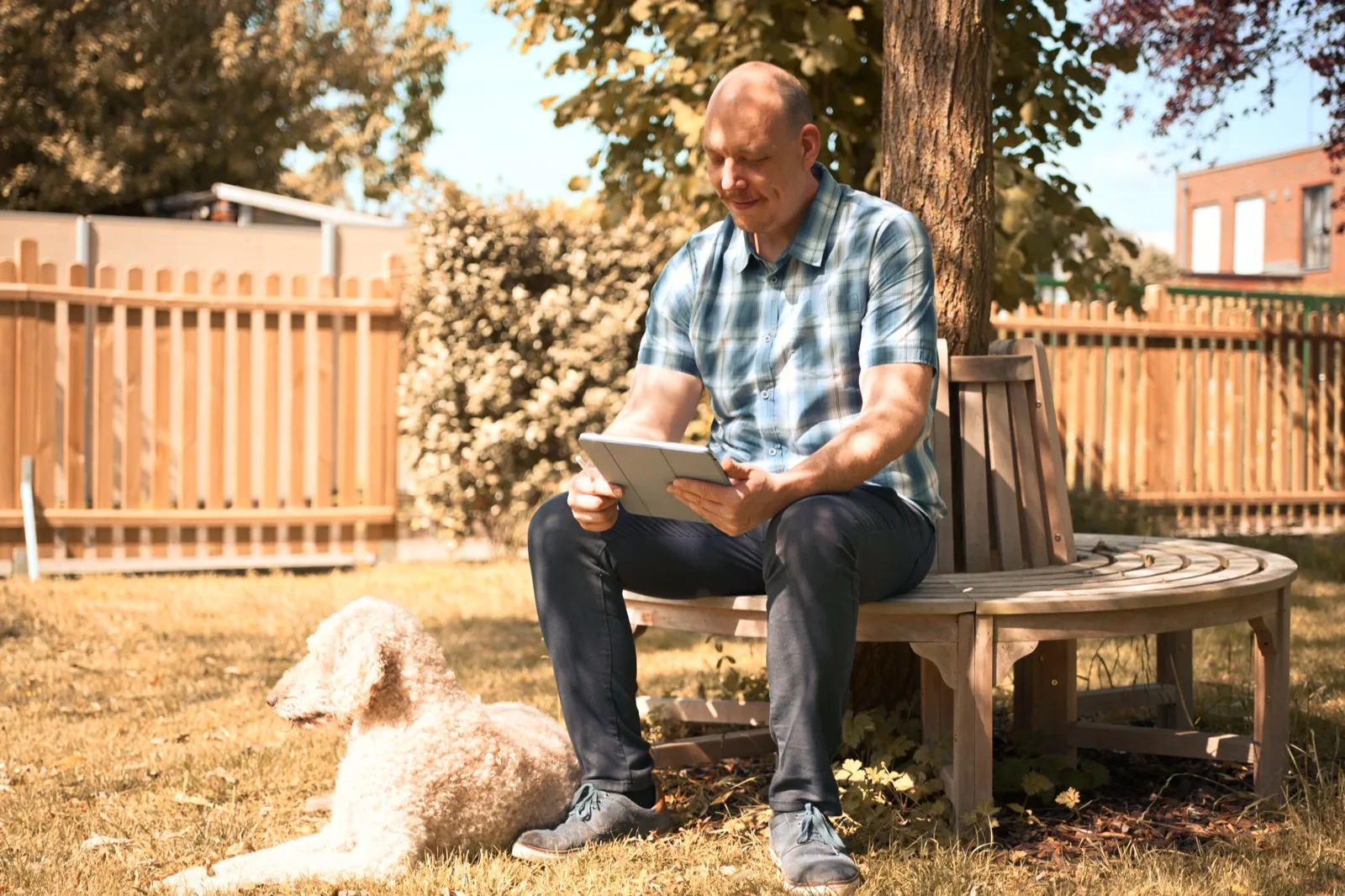 Dustin Dondrup mit Tablet auf der Gartenbank, daneben sein Hund